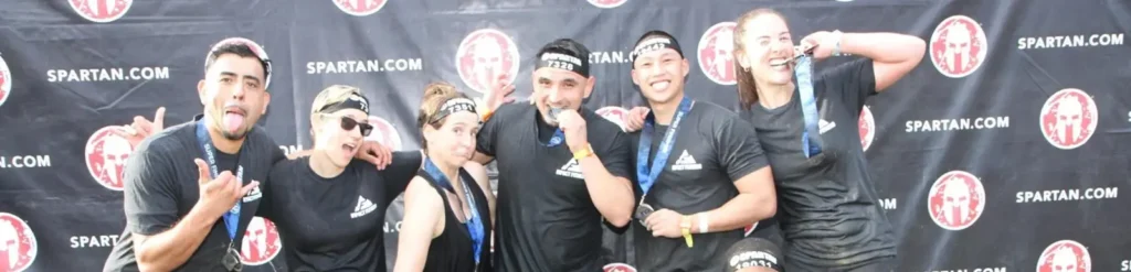 Impact Fitness Oakland strength and conditioning group celebrating with finisher medals at a Spartan Race obstacle event
